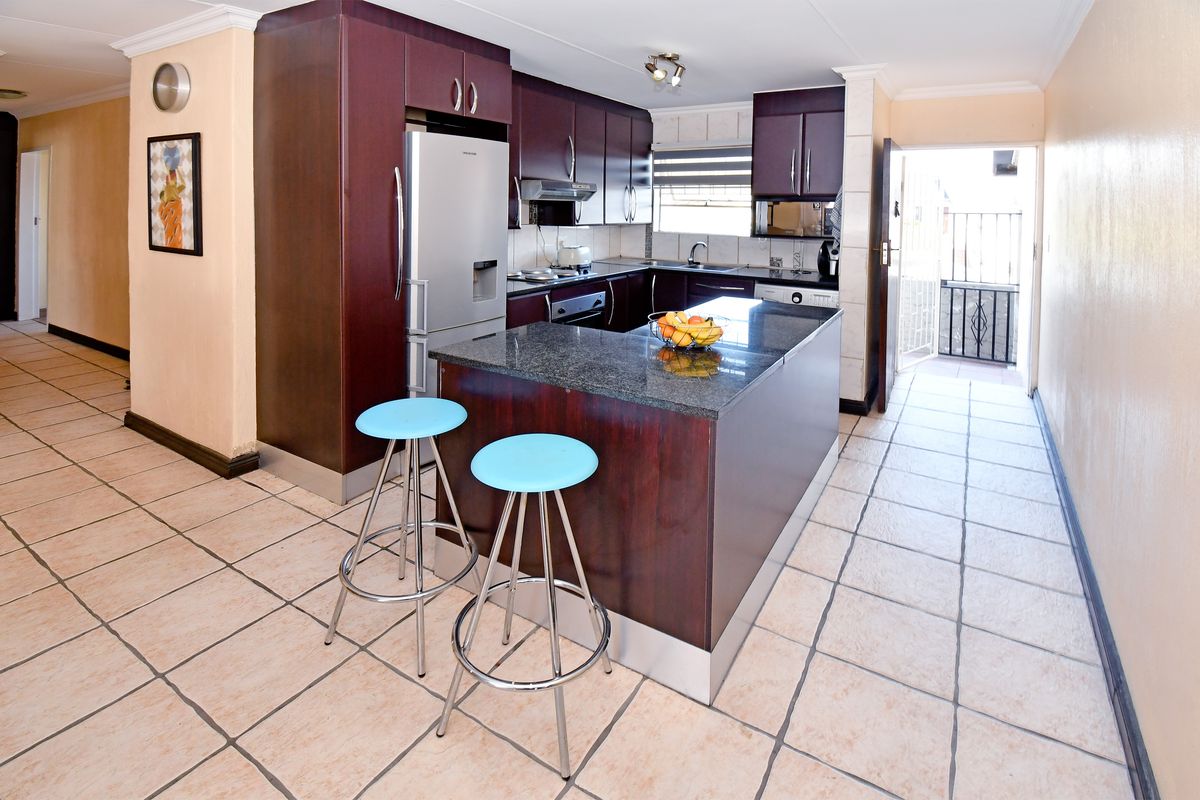 A functional kitchen featuring dark wood cabinetry, granite countertops, a central island, and tiled flooring, with direct access to an outdoor area.