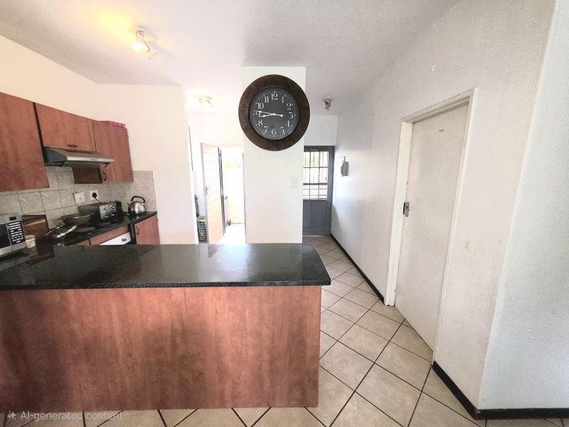 Open-plan kitchen area featuring granite countertops, built-in cabinetry, and tiled flooring, leading to a hallway with access to exterior security gates.