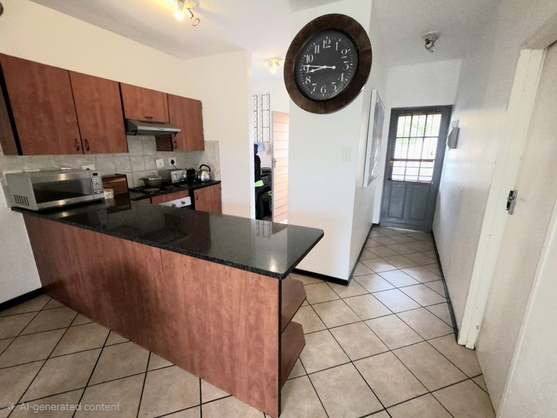 A functional kitchen featuring granite countertops, laminate cabinetry, and tiled flooring, with an adjacent hallway leading to a secure exterior door.