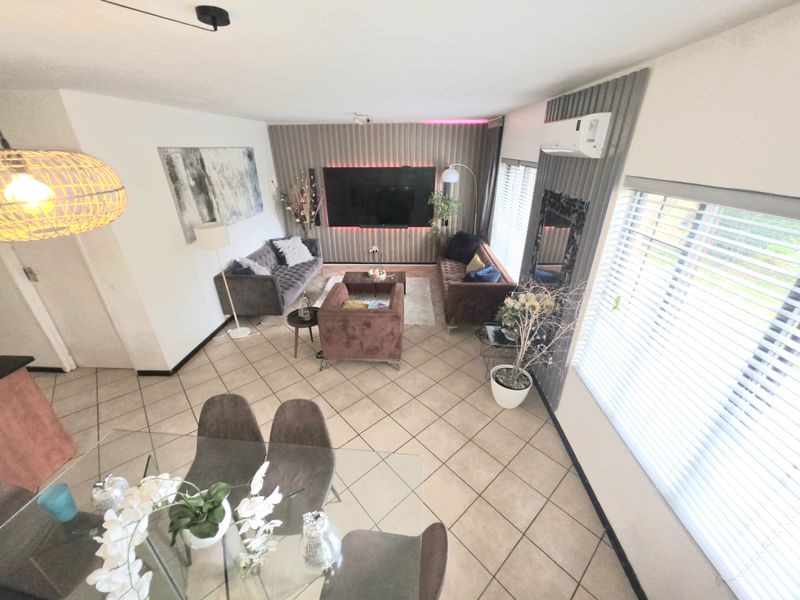 Spacious open-plan living and dining area featuring tiled floors, a feature wall with integrated lighting, and wall-mounted air conditioning.