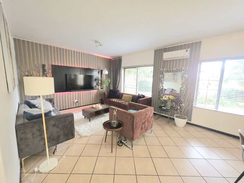 A spacious living room featuring tiled flooring, a decorative feature wall with integrated lighting, and a wall-mounted air conditioning unit.