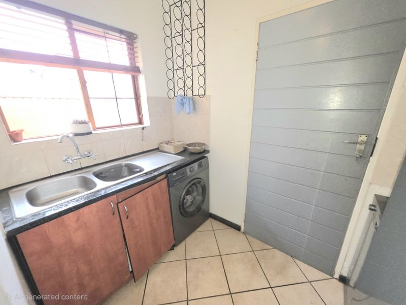 A functional laundry area featuring a double stainless steel sink, laminate cabinetry, tiled splashback, and tiled flooring with direct access to an internal door.