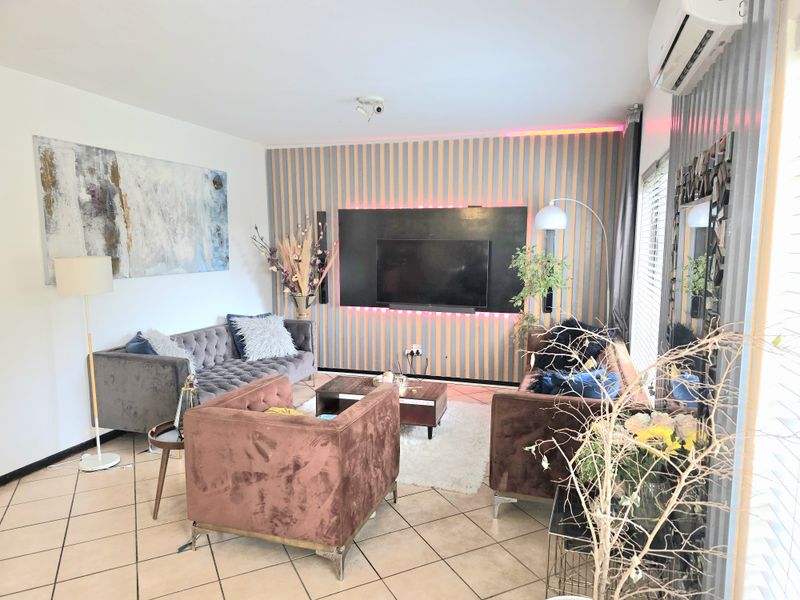 A modern living room featuring tiled flooring, a decorative feature wall with integrated lighting, and a wall-mounted split-system air conditioner.