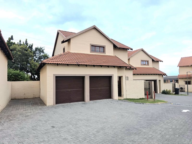 Front view of a townhouse featuring a double garage, tiled roof, and paved driveway within a secure complex setting.