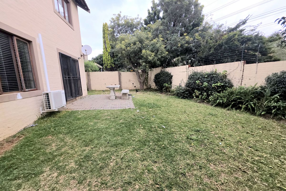A private rear garden featuring a paved patio area, established landscaping, and secure perimeter walling with electric fencing.