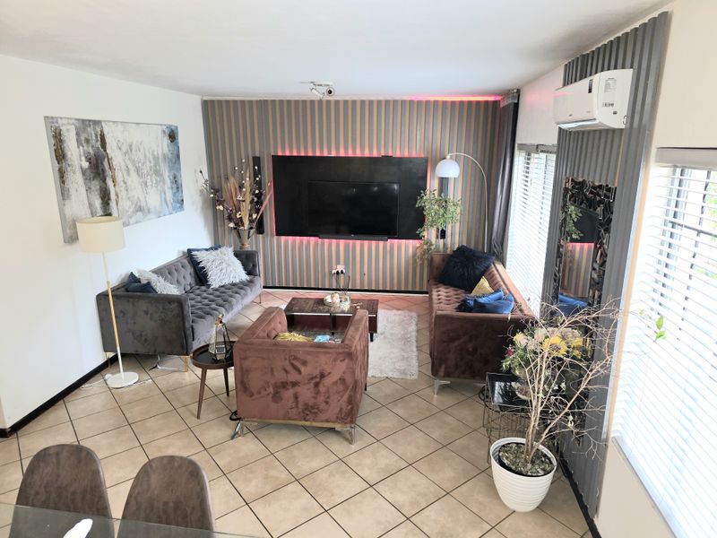 A well-maintained living room featuring a modern slatted feature wall with integrated lighting, tiled flooring, and a wall-mounted air conditioning unit.