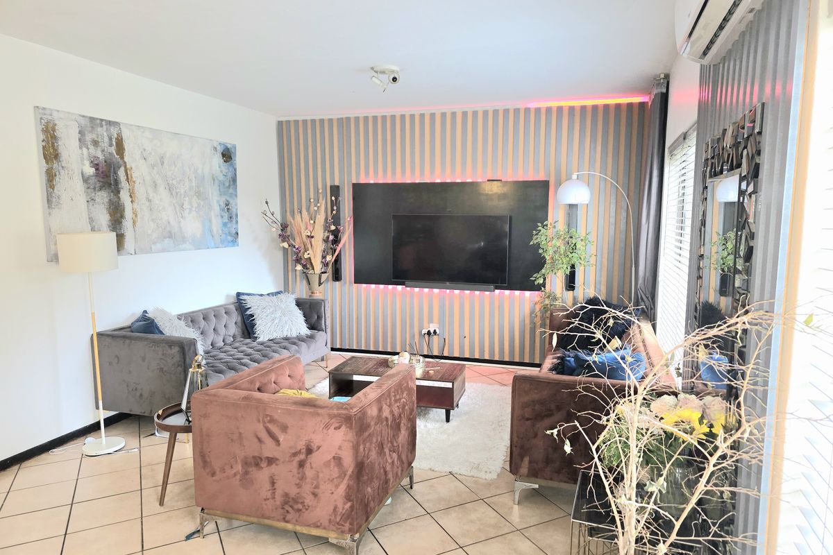 A modern living room featuring tiled flooring, a decorative feature wall with integrated lighting, and a wall-mounted split-system air conditioner.