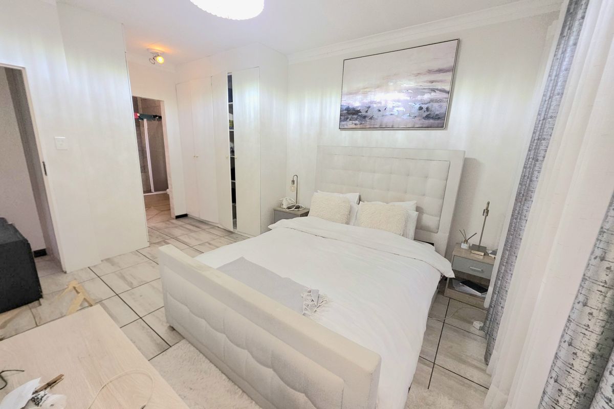 A bright bedroom featuring tiled flooring, built-in cupboards, and coved ceiling details, offering a clean and functional living space.