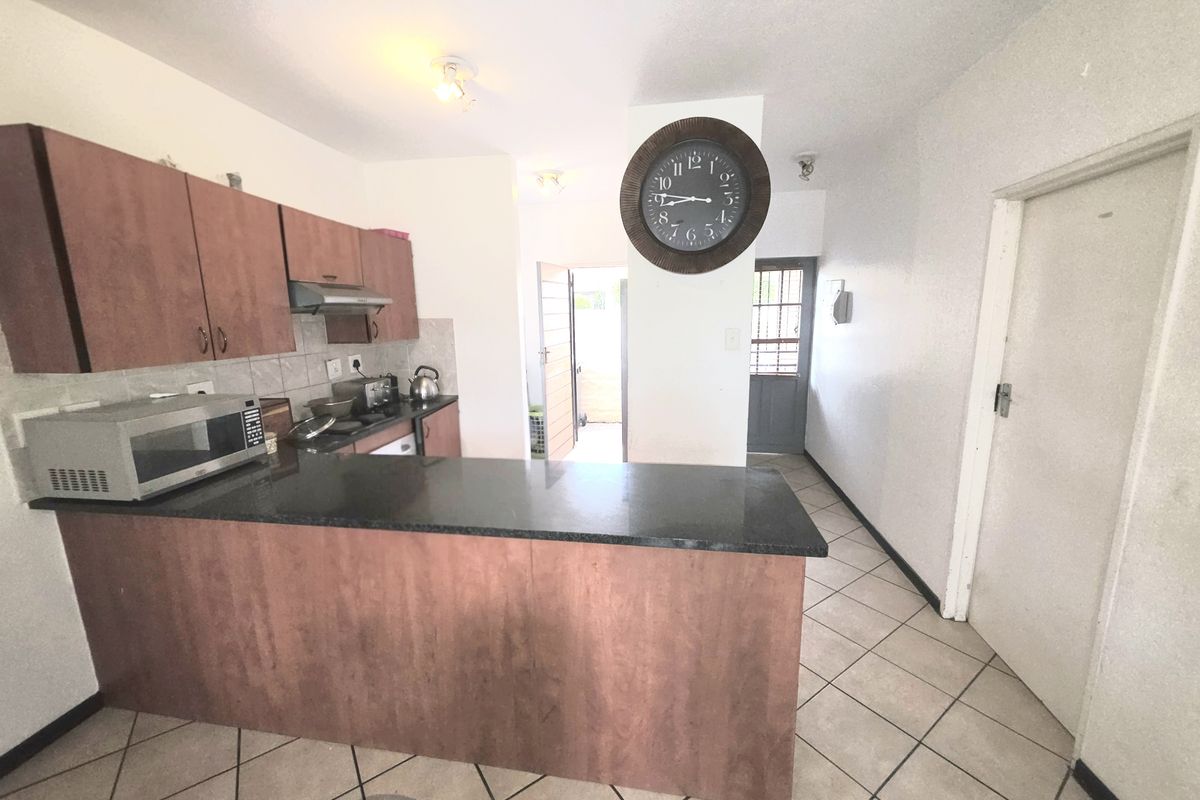 Functional kitchen featuring laminate cabinetry, granite countertops, and tiled flooring, with an open-plan layout leading to an exterior entrance.