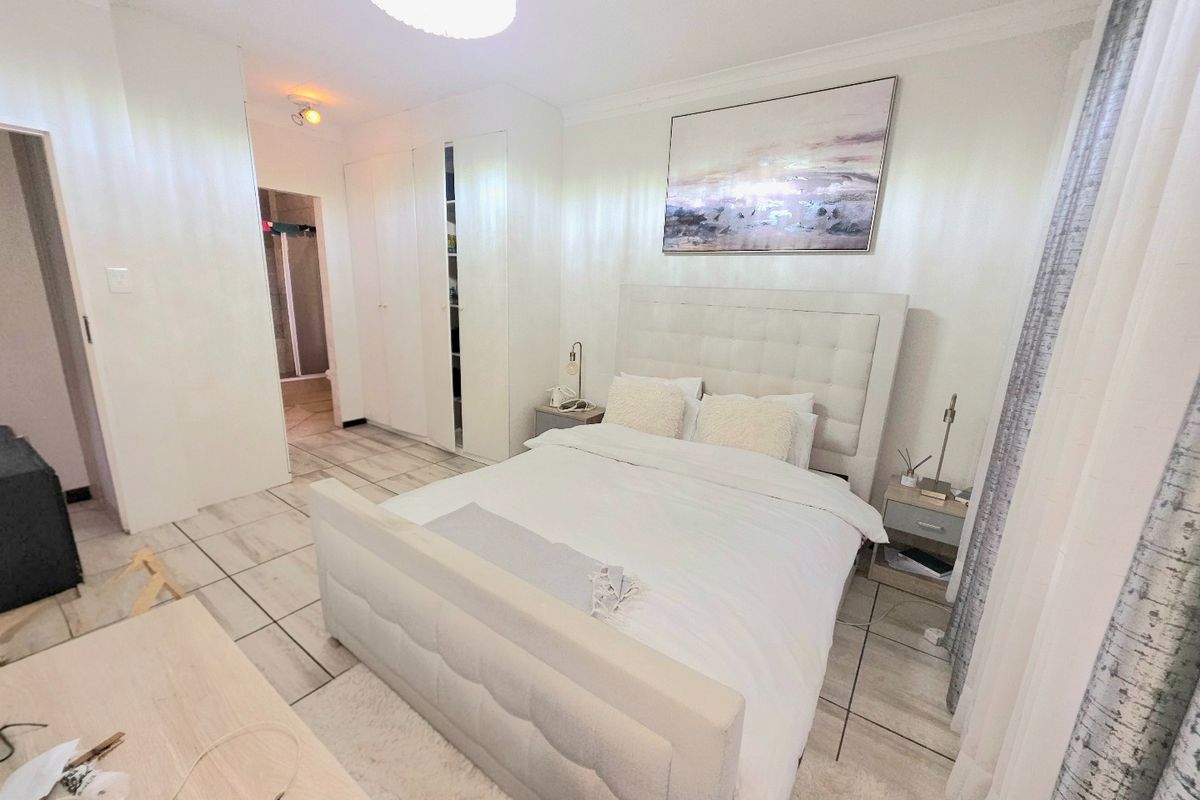 A well-maintained bedroom featuring neutral tiled flooring, built-in cupboards, and decorative ceiling cornice, offering a clean and functional living space.