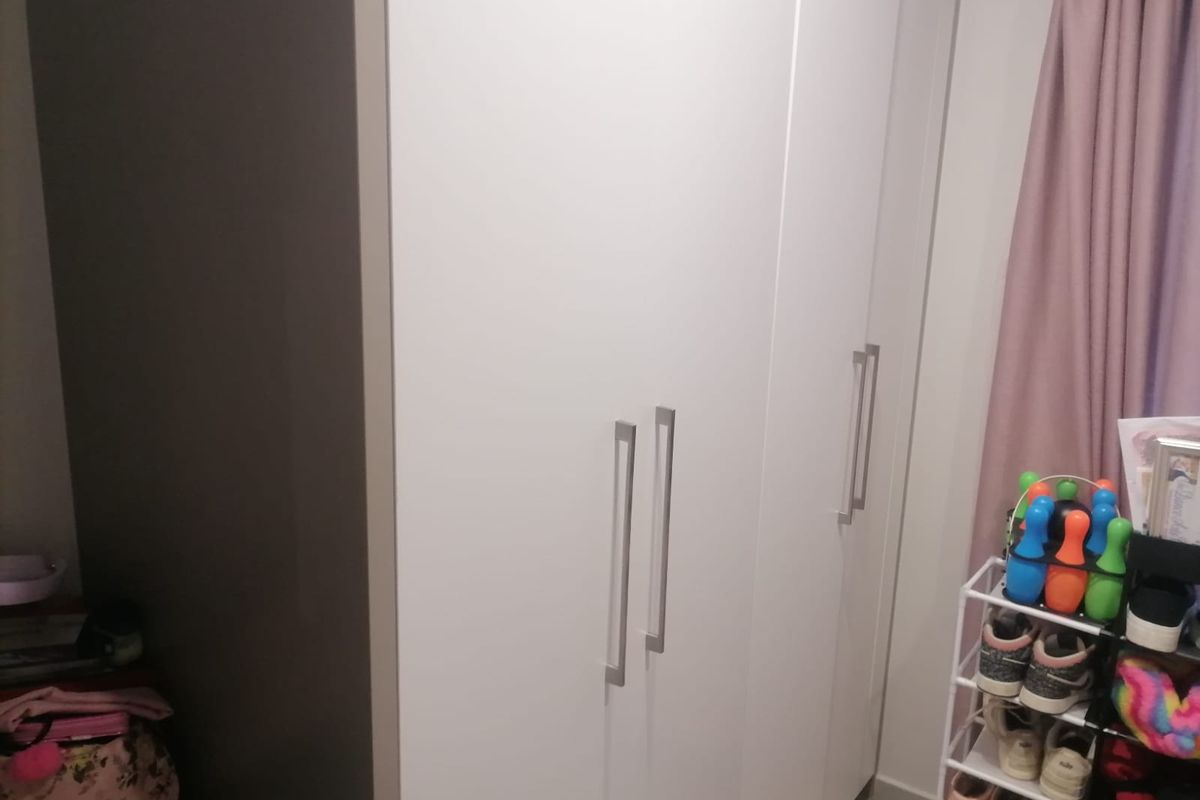 A bedroom featuring a modern white built-in wardrobe with sleek vertical handles.