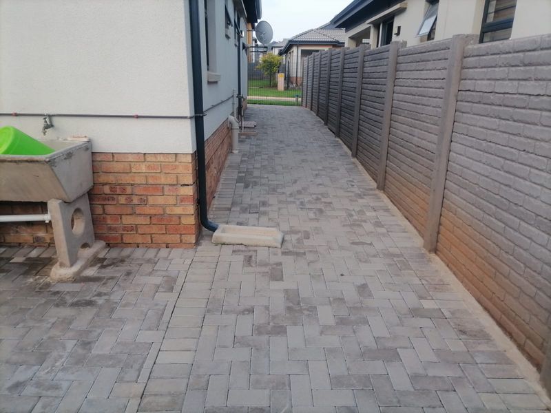 A side pathway featuring paved flooring, a precast concrete boundary wall, and an external utility wash basin.
