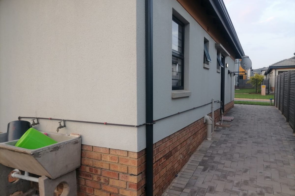 Side exterior view of the house featuring a paved walkway, brick plinth, rendered walls, and a functional concrete laundry trough with external water taps.