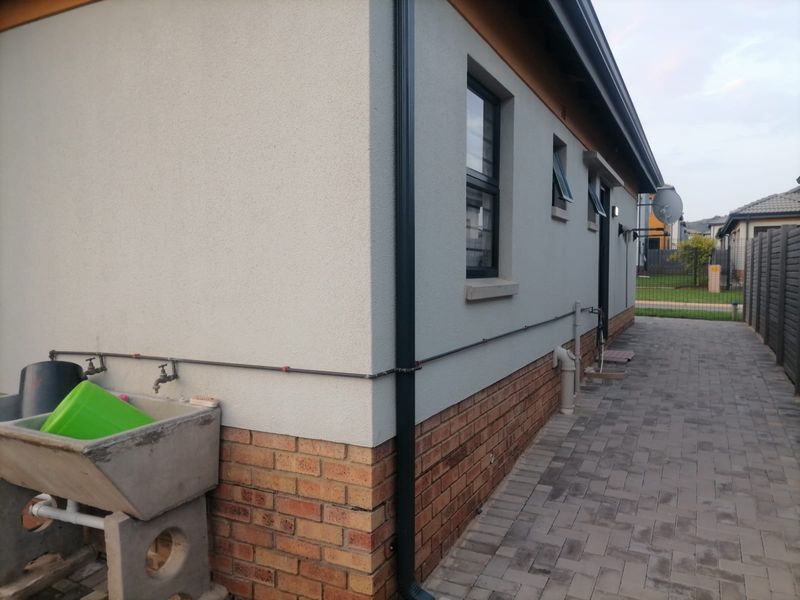 Side exterior view of the house featuring a paved walkway, brick plinth, rendered walls, and a functional concrete laundry trough with external water taps.