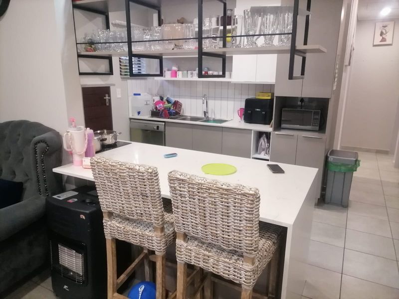 Modern kitchen featuring a central island with quartz countertops, integrated dishwasher, stainless steel sink, and stylish overhead shelving with a tiled backsplash.