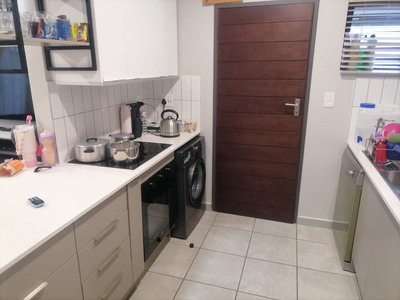 A functional kitchen featuring modern cabinetry, stone countertops, subway tile backsplash, and integrated appliances including a washing machine and dishwasher.