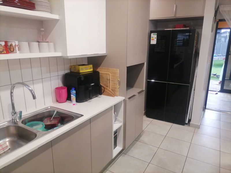 A functional kitchen featuring modern neutral cabinetry, a double bowl stainless steel sink, tiled splashback, and tiled flooring with direct access to the outdoor area.