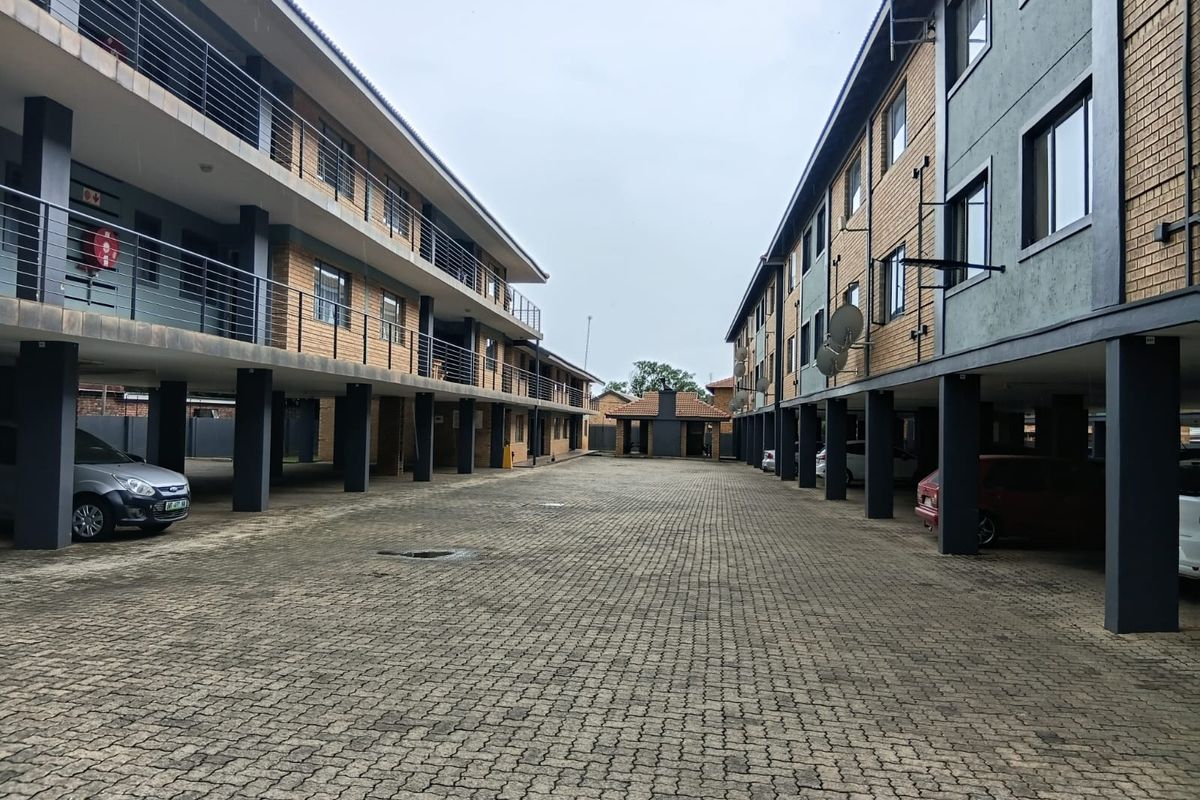 View of the apartment complex courtyard featuring paved parking area, covered bays, and multi-story residential blocks with balconies.