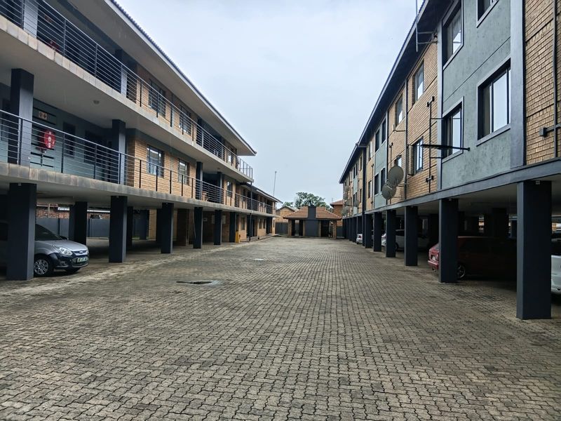 View of the apartment complex courtyard featuring paved parking area, covered bays, and multi-story residential blocks with balconies.