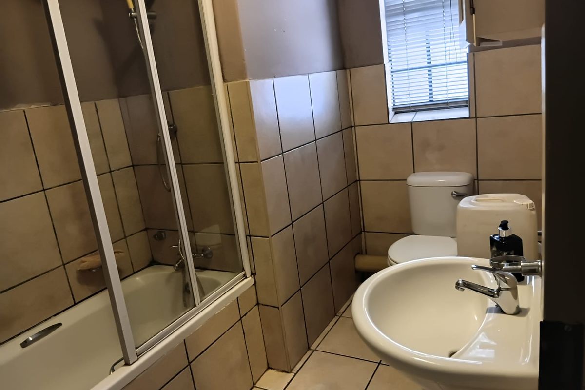 A functional bathroom featuring a pedestal basin, toilet, and a shower-over-bath combination with tiled finishes throughout.