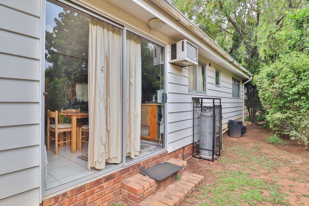 Rear exterior view of the property featuring weatherboard cladding, a sliding glass door, and a secure gas cylinder storage cage.