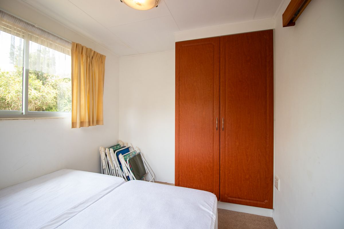A functional bedroom featuring a built-in wooden wardrobe, carpeted flooring, and a sliding window providing natural light.