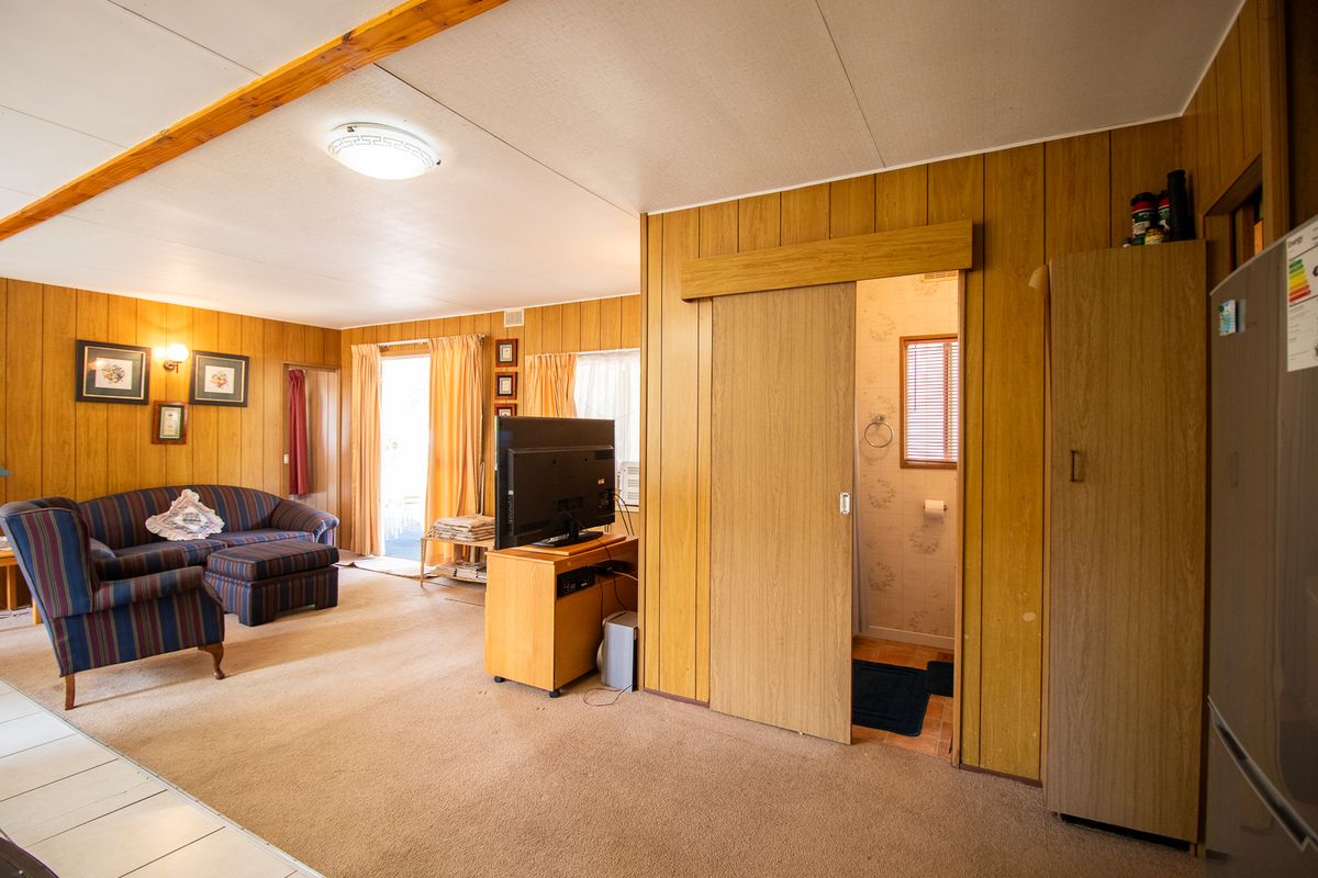 A living room featuring dated wood paneling, carpet flooring, and a sliding door leading to an adjacent bathroom area.
