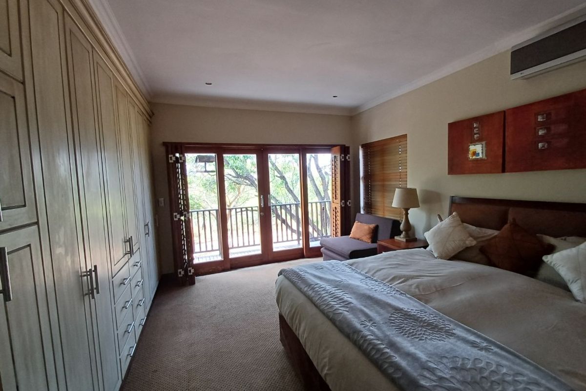 Spacious bedroom featuring extensive built-in cabinetry, carpeted flooring, and large wooden doors opening onto a private balcony with natural views.