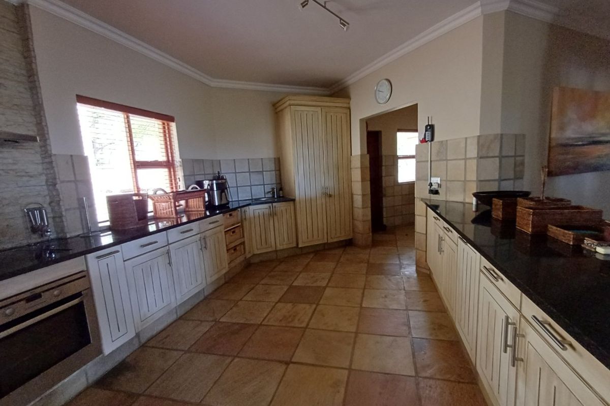 Spacious kitchen featuring granite countertops, built-in oven, ample cabinetry, and terracotta-style floor tiles, offering a functional layout with a separate scullery area.