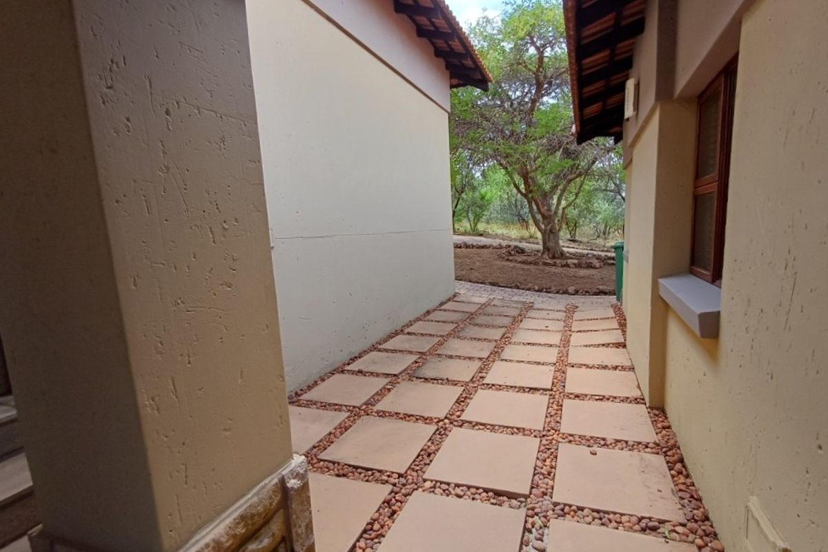 A side walkway featuring paved stone tiles with decorative pebble borders, connecting the front and rear exterior areas of the property.