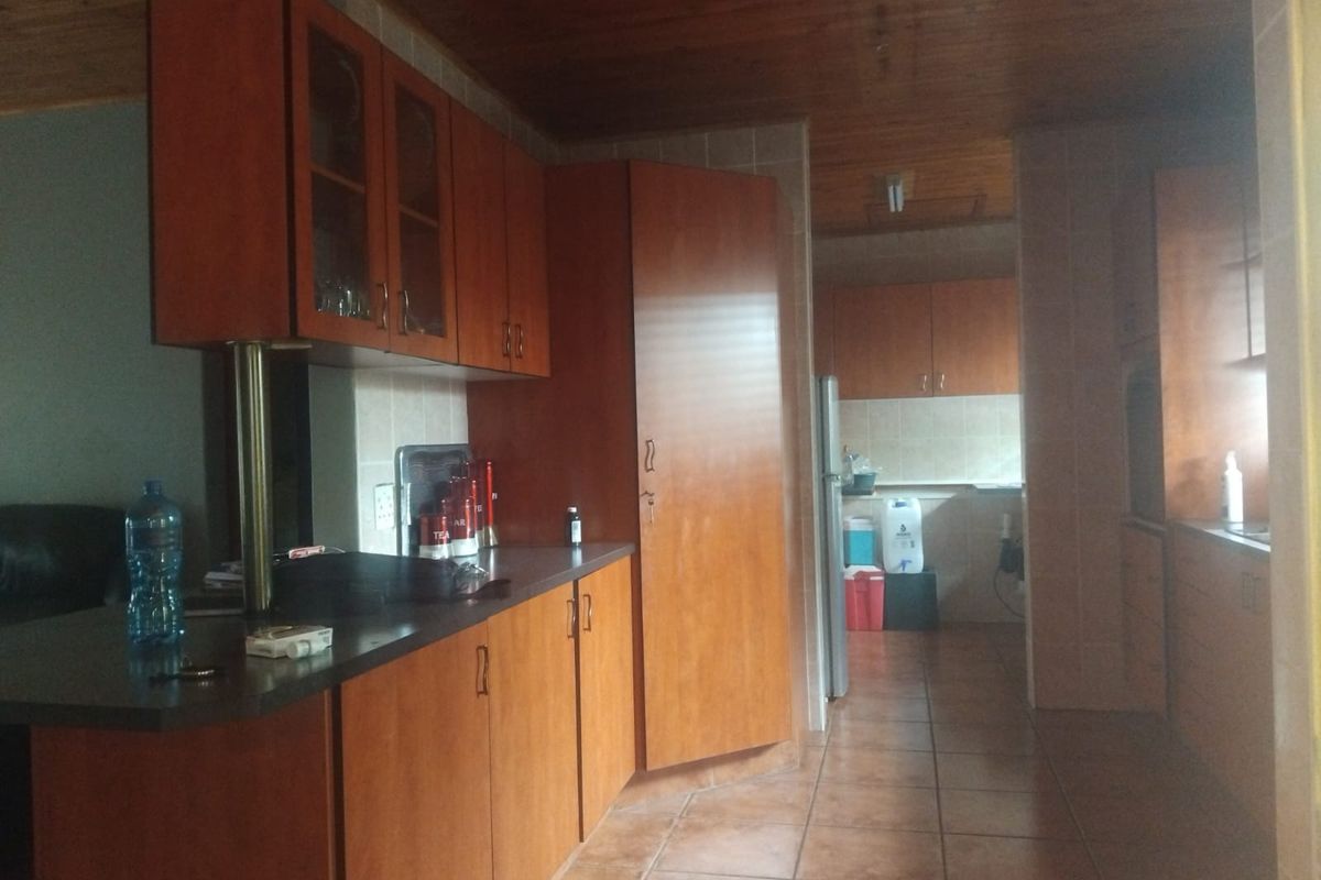 A functional kitchen featuring timber cabinetry, tiled flooring, and a wood-paneled ceiling, with an adjacent scullery area providing additional storage and workspace.