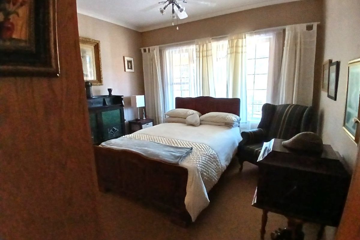 A standard bedroom featuring carpeted flooring, a ceiling fan, and large windows allowing natural light into the space.