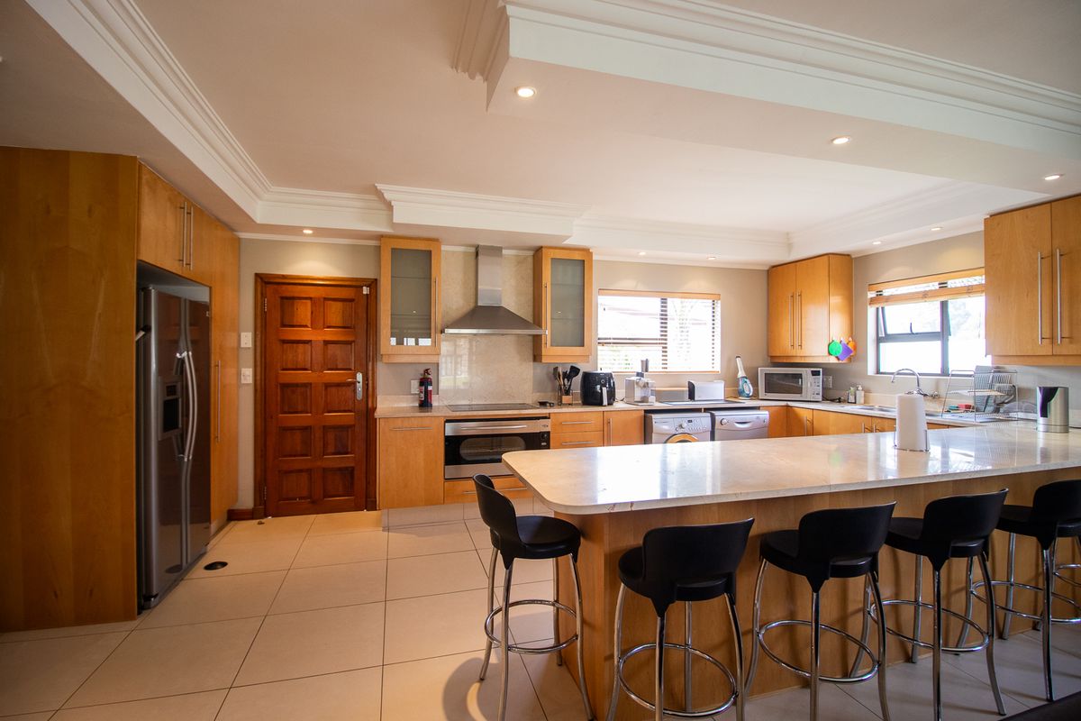 Spacious kitchen featuring light wood cabinetry, a large central island with breakfast bar seating, stone countertops, and integrated appliances.