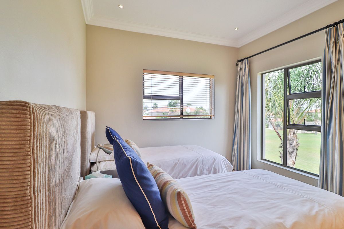 A well-maintained bedroom featuring recessed downlights, decorative cornicing, and large aluminium-framed windows with venetian blinds, offering natural light and garden views.