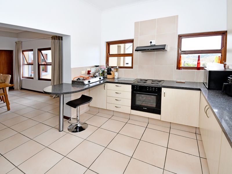 Open plan kitchen featuring light-toned cabinetry, dark laminate countertops, built-in oven and hob, and tiled flooring, seamlessly connecting to the adjacent dining area.
