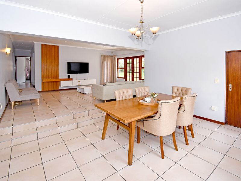 Spacious open-plan living and dining area featuring tiled flooring, neutral walls, and a built-in media unit with timber accents.