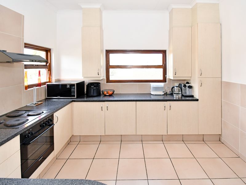 A functional kitchen featuring light-toned built-in cabinetry, dark laminate countertops, an electric hob, built-in oven, and tiled finishes throughout.