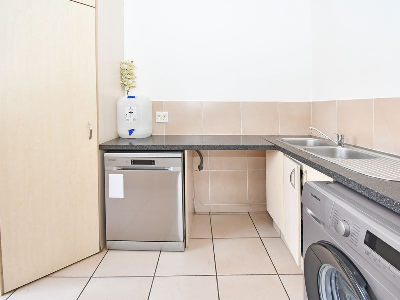 A functional scullery area featuring granite countertops, a double stainless steel sink, tiled splashbacks, and dedicated space for laundry and kitchen appliances.