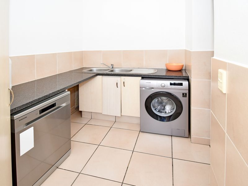 A functional laundry area featuring tiled flooring, granite countertops, a stainless steel sink, and built-in cabinetry for organized storage.