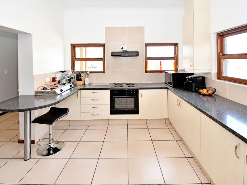 A functional kitchen featuring granite countertops, built-in oven, electric hob, extractor fan, and a breakfast bar with tiled flooring throughout.