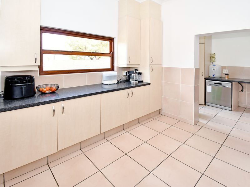 A functional kitchen featuring light wood-tone cabinetry, dark granite countertops, tiled splashbacks, and ceramic floor tiles, with an adjoining scullery area.