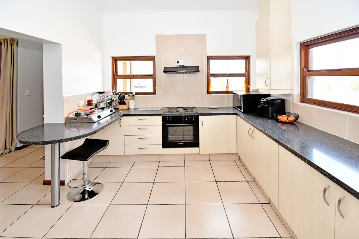 A functional kitchen featuring granite countertops, built-in oven, electric hob, extractor fan, and a breakfast bar with tiled flooring throughout.