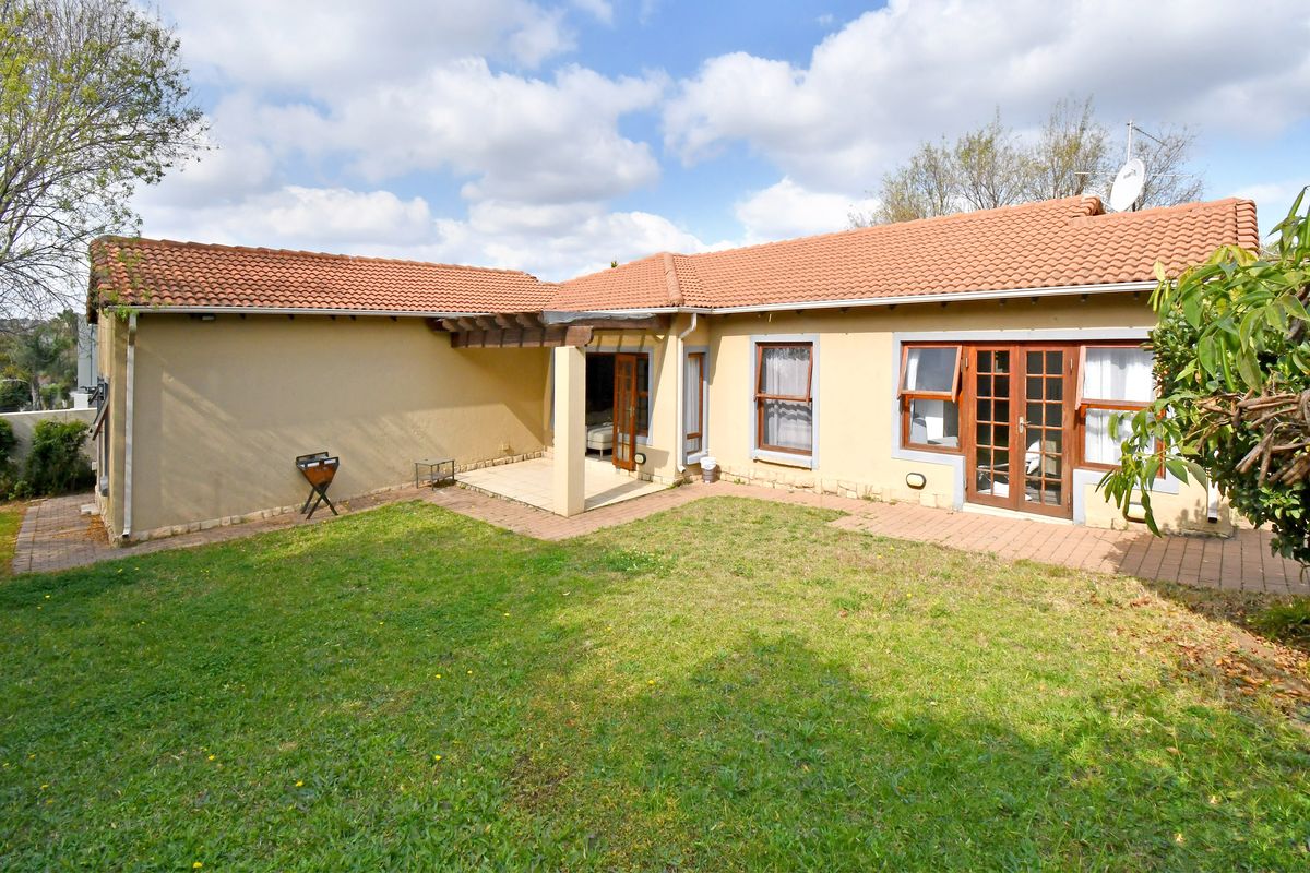 Rear view of the house featuring a covered patio with a timber pergola, paved areas, and access through timber-framed french doors to the garden.