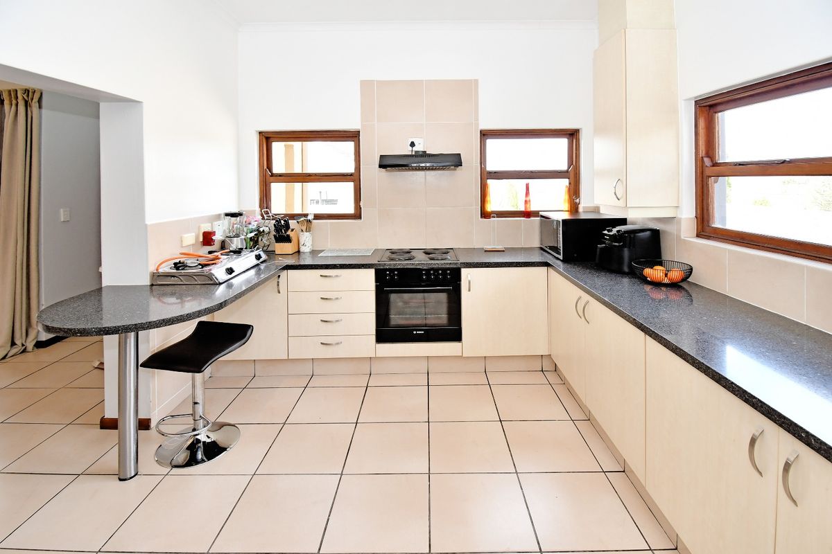 A functional kitchen featuring light-toned cabinetry, dark granite countertops, a breakfast bar, and tiled flooring with integrated oven and hob.