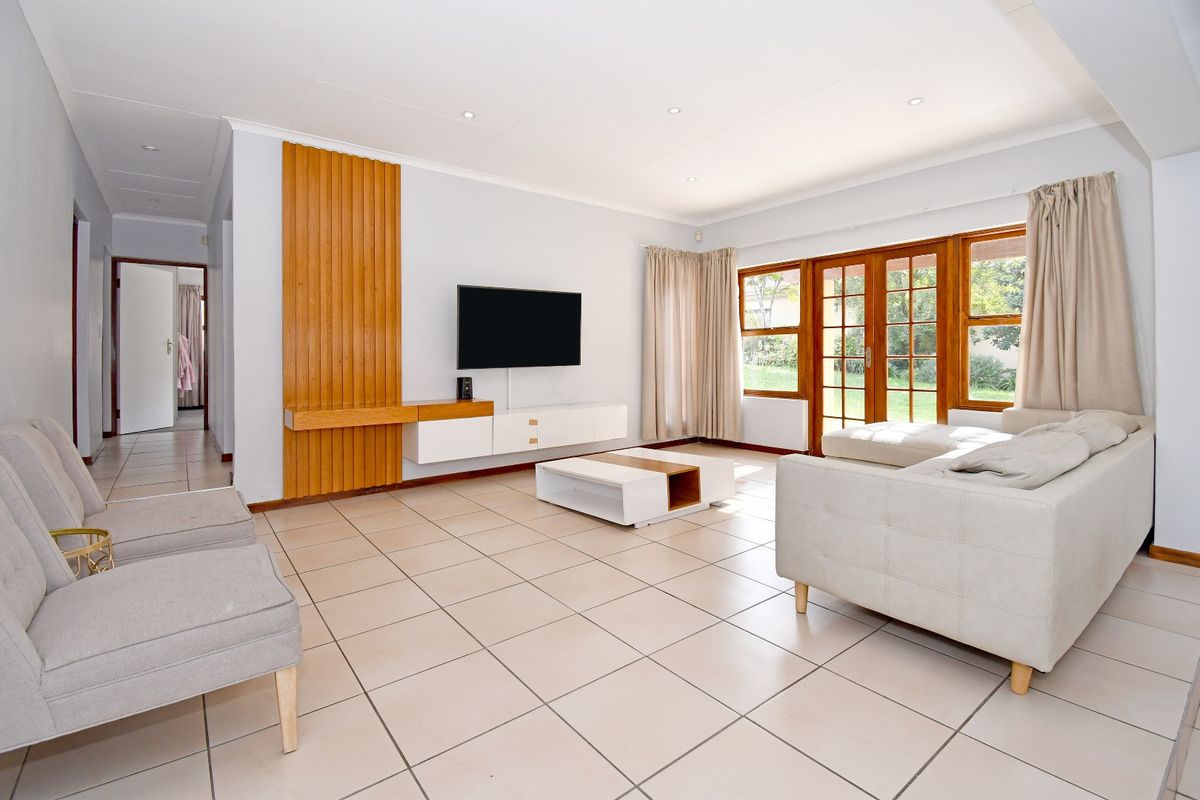Spacious living room featuring neutral tiled flooring, recessed lighting, and a feature timber wall panel with integrated media storage, opening to the garden.