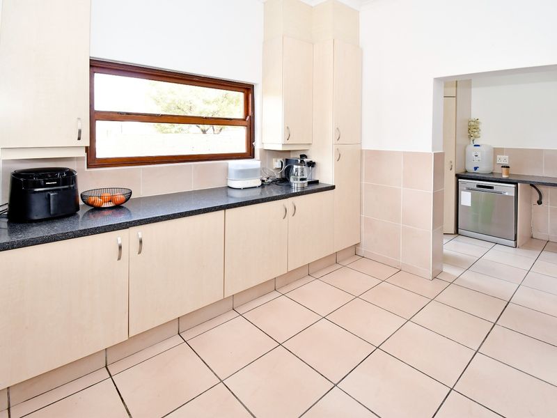 A functional kitchen featuring light wood-tone cabinetry, dark granite countertops, tiled splashbacks, and ceramic floor tiles, with an adjoining scullery area.