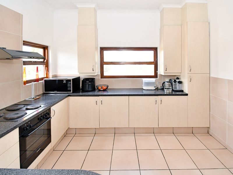 A functional kitchen featuring light-toned cabinetry, dark laminate countertops, a built-in oven with hob, and tiled flooring throughout.