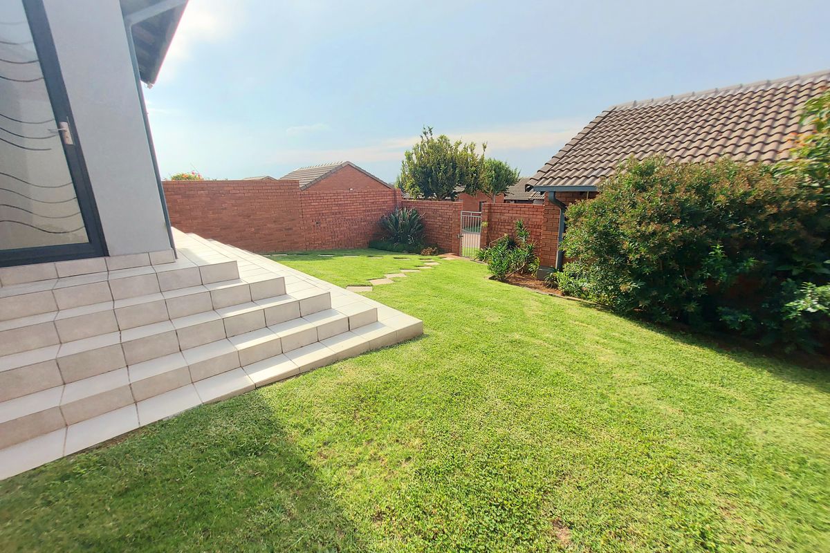 A private rear garden featuring a well-maintained lawn, paved steps leading to the dwelling, and perimeter brick boundary walls.