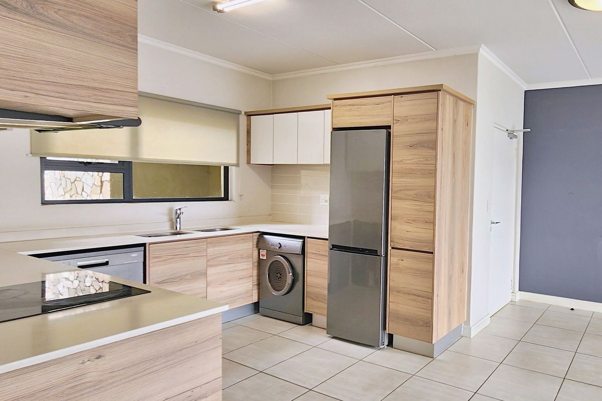Modern kitchen featuring wood-grain cabinetry, stone countertops, integrated sink, and built-in appliances, set against a neutral tiled floor.