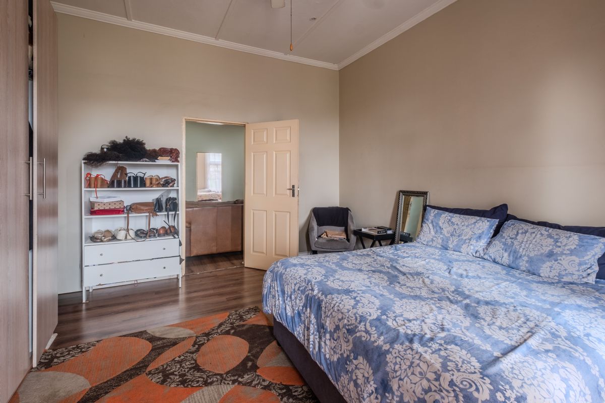 A bedroom featuring laminate flooring, a built-in wardrobe, and a ceiling fan, with an adjoining room visible through the doorway.